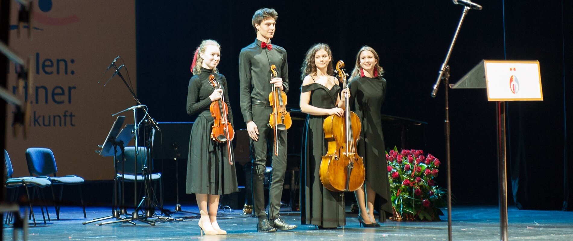 Zdjęcie sceny opery i filharmonii podlaskiej na której stoją 4 osoby. 3 z nich trzymają instrumenty muzyczne.